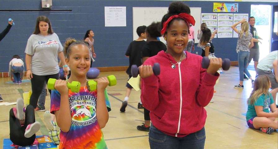 Two students in gym class lifting weights.